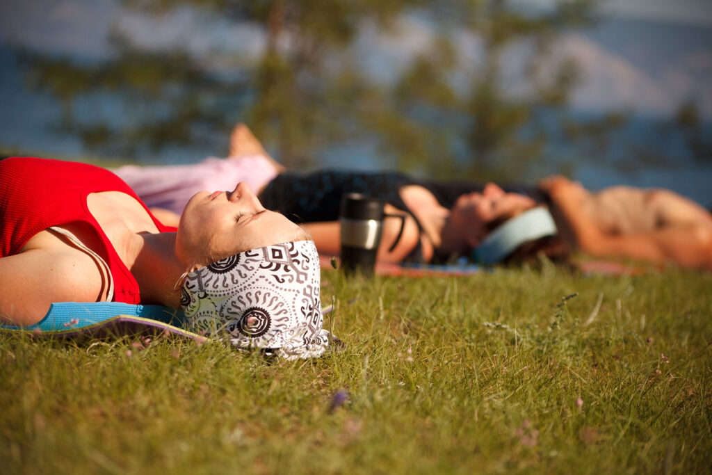 Two women laying down in the grass relaxing on yoga mats