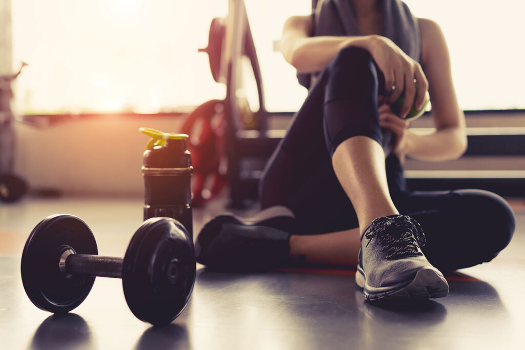 Gym water bottle next to a woman wearing shoes sitting beside a hand weight